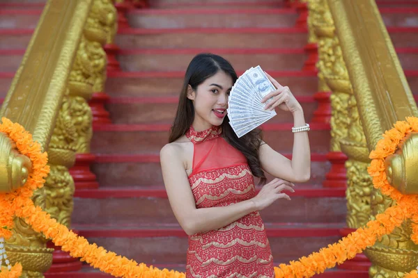 Young happy Asian woman holding lots of money US dollar in Chinese New Year