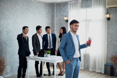 İş adamı mutlu gururla kupa tutuyor ve iş adamları da onu kıskanıyor.