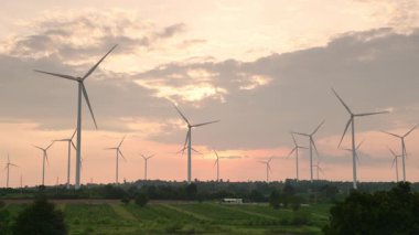 Elektrik üretim istasyonu, günbatımında tarımsal alanlarda rüzgar türbinleri güç jeneratörü, Alternatif Enerji Yel Değirmeni Çiftliği, yemyeşil alanlar arasında yenilenebilir enerji üretimi, temiz enerji kavramı.