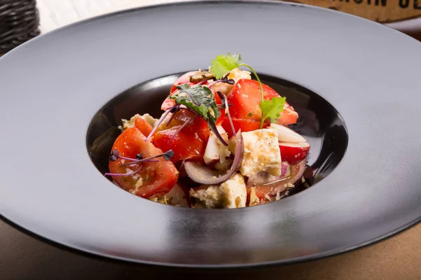 Siyah bir tabak içinde domates ve beyaz peynirli salata servis