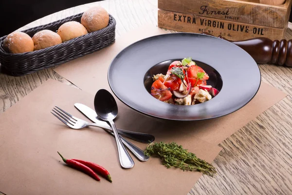 Siyah bir tabak içinde domates ve beyaz peynirli salata servis