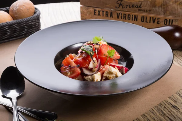 Siyah bir tabak içinde domates ve beyaz peynirli salata servis