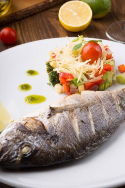 Ahşap masa üzerinde sebze salatası ile servis ızgara dorado balık