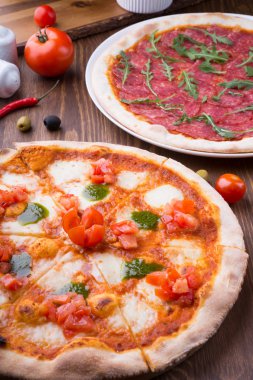 İki farklı pizza taze pişmiş ve ahşap masaya servis