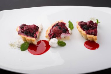 Beyaz tabakta servis edilen farklı meyveli tartlar.