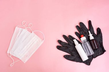 Tıbbi koruyucu maske ve pembe arka planda izole edilmiş siyah eldivenlerdeki antiseptik şişeler. Sağlık sigortası Coronavirüs Karantinası