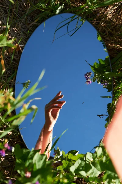 Hand in the mirror on the grass. Reflection