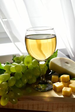Pencerenin yanında meyve ve peynirli bir bardak beyaz şarap.