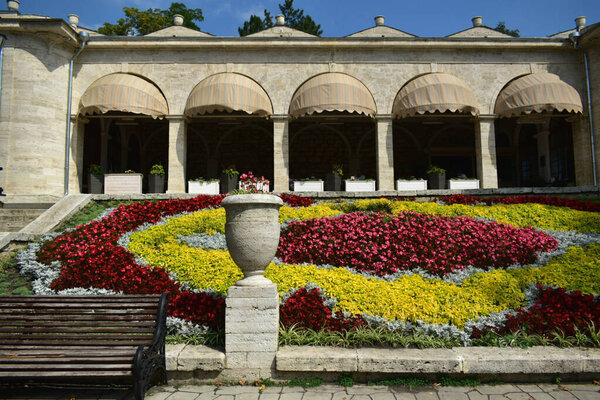 Красивый пейзаж с вазой из камня с цветами на фоне клумбы и здания Академической галереи в ясный летний день в Пятигорске.
