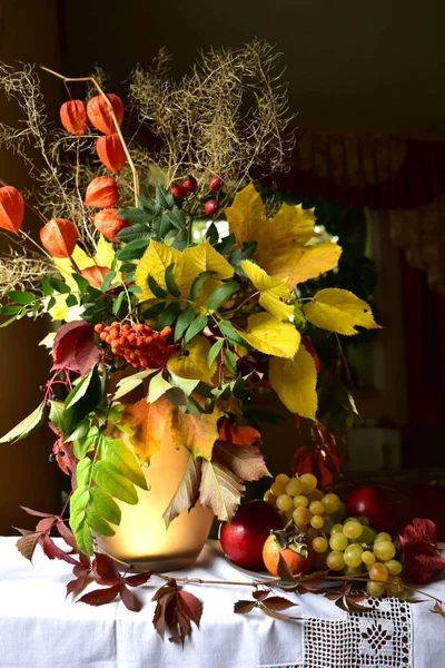 Stillleben mit Früchten und einer Vase mit einem Strauß von Herbstblättern und Beeren auf dunklem Hintergrund. — Stockfoto