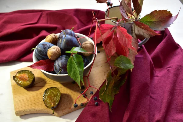 Ripe plums and walnuts with a branch of wild grapes on the table. — Stock Photo, Image