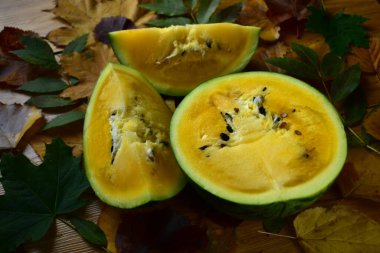 Sonbahar yapraklarıyla ahşap bir masada sarı karpuz kes.