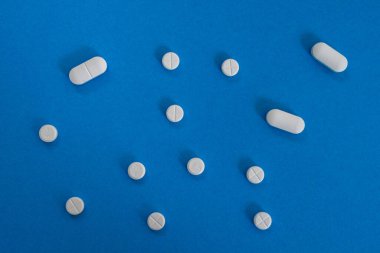 Mavi arkaplanda beyaz yuvarlak ve oval tabletlerin üst görünümü