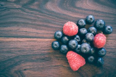 Ahşap zemin üzerinde ahududu ve yaban mersinlerinin panoramik yakın çekimi. Metin için üst görünüm ve kopyala