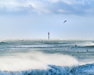 Fırtınada deniz feneri ve martılar uçuyor. Mavi, gökyüzü ve beyaz bulutlar