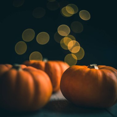 Koyu arkaplanda üç küçük balkabağı, sarı bokeh ışığı