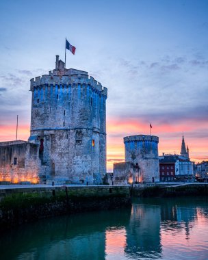 Gün batımında meşhur eski kuleleriyle La Rochelle 'in eski limanı. Güzel turuncu gökyüzü. portre biçimi