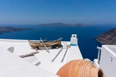 Arka planda mavi Akdeniz olan Santorini 'nin çatı manzarası. Çerçevede eski ahşap tekne ve amfora.