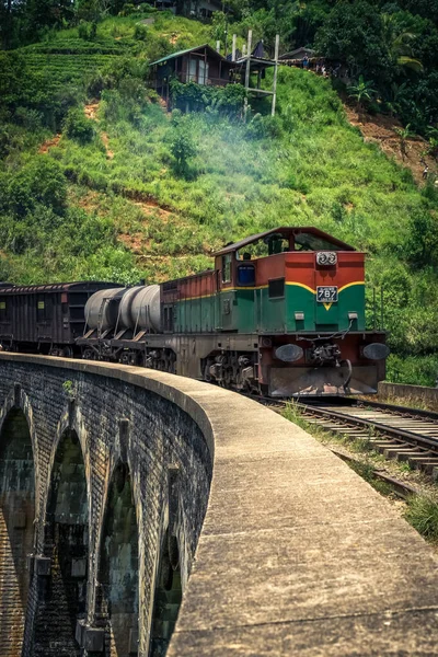 Green and red train on the famous nine arches Bridge in highlands near Ella, Sri Lanka. Jungle and tea plantation all around.