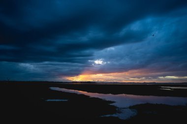 Suyun üzerinde fırtına bulutları, gölün üzerinde gün batımı, turuncu güneş ışığı, bulutlu dramatik gökyüzü. Sudaki güzel yansımalar