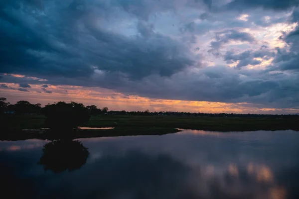 Storm clouds over the water with the sunset over the lake, orange sunlight, dramatic sky with clouds. Beautiful reflections in water