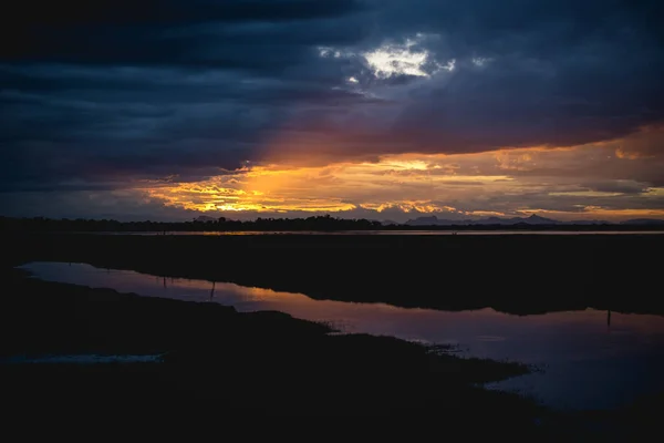 Storm clouds over the water with the sunset over the lake, orange sunlight, dramatic sky with clouds. Beautiful reflections in water