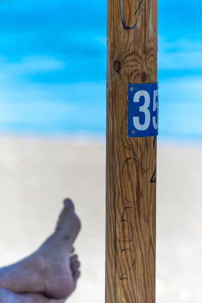 wooden sign on the beach. number 35. feet on the background