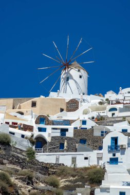 Santorini adasındaki Oia kasabasının panoramik manzarası, güneşli bir günde Yunanistan 'ın eski beyaz yıkanmış evleri ve geleneksel yel değirmeniyle