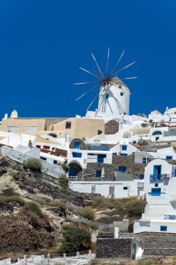 Santorini adasındaki Oia kasabasının panoramik manzarası, güneşli bir günde Yunanistan 'ın eski beyaz yıkanmış evleri ve geleneksel yel değirmeniyle