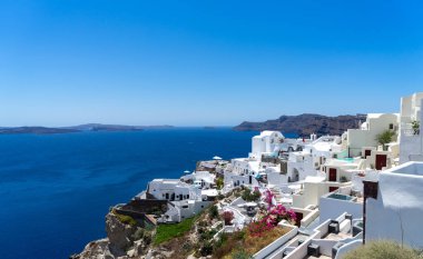 Santorini adasındaki Oia kasabasının panoramik manzarası, güneşli bir günde Yunanistan 'ın eski beyaz yıkanmış evleri ve geleneksel yel değirmeniyle
