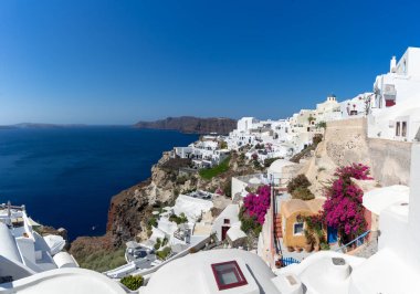 Santorini adasındaki Oia kasabasının panoramik manzarası, güneşli bir günde Yunanistan 'ın eski beyaz yıkanmış evleri ve geleneksel yel değirmeniyle