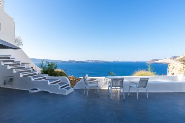 Güneşli bir günde, beyaz terasta mavi deniz ve kaldera manzaralı, insansız dört beyaz sandalye. Oia, Santorini Adası, Yunanistan