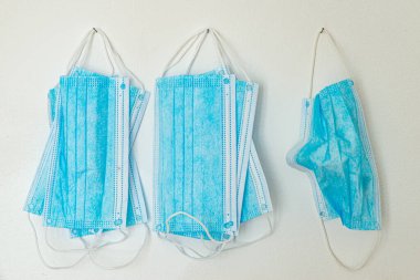 Mavi cerrahi maskeler, beyaz duvarda asılı.