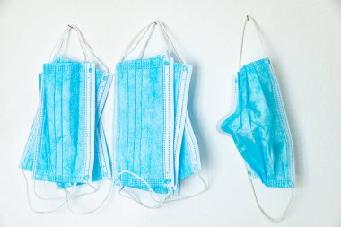 Mavi cerrahi maskeler, beyaz duvarda asılı.