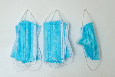 Mavi cerrahi maskeler, beyaz duvarda asılı.