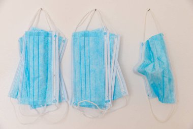 Mavi cerrahi maskeler, beyaz duvarda asılı.