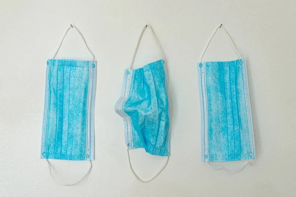 Mavi cerrahi maskeler, beyaz duvarda asılı.