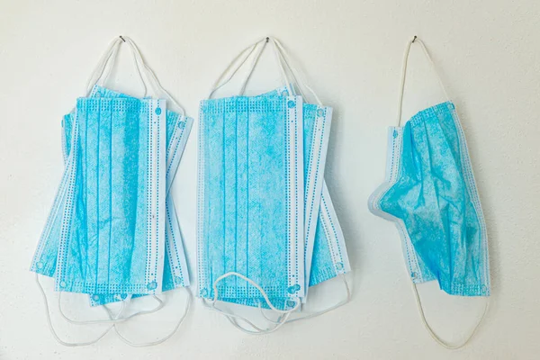 Mavi cerrahi maskeler, beyaz duvarda asılı.