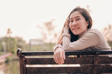 Mutlu yüzlü bir kadın, güneşli yaz gününde parkta bankta oturup rahatlıyor. Açık havada. Doğa.