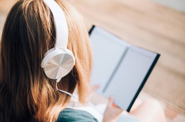 Gözlüklü gülümseyen kadın kitap okuyor ve kulaklıkla müzik dinliyor. Dışarıda, güneş ışığına karşı, şehir yaşam tarzı konseptine karşı..