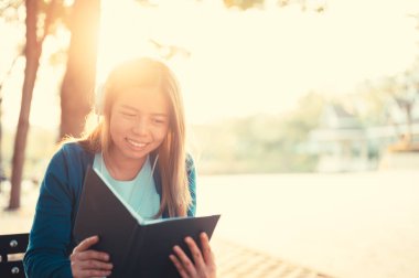 Gözlüklü gülümseyen kadın kitap okuyor ve kulaklıkla müzik dinliyor. Dışarıda, güneş ışığına karşı, şehir yaşam tarzı konseptine karşı..