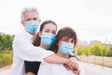 Yeni normal. Maskeli aile kucaklaşması. Aile üyeleri birbirlerine koruyucu maskelerle sarılırlar. Koronavirüse karşı maskeli bir aile. Güvenlik ve salgın konsepti. Coronavirus. Sosyal uzaklık.