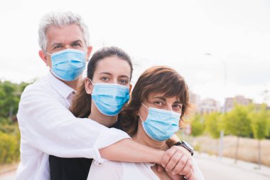 Yeni normal. Maskeli aile kucaklaşması. Aile üyeleri birbirlerine koruyucu maskelerle sarılırlar. Koronavirüse karşı maskeli bir aile. Güvenlik ve salgın konsepti. Coronavirus. Sosyal uzaklık.