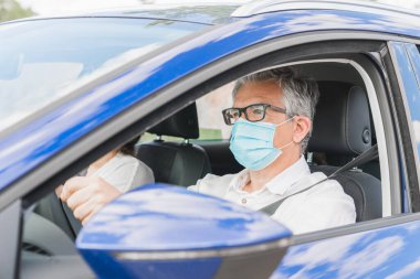 Yeni normal. Tıbbi maskeli bir sürücü bir yolcuyla araba kullanıyor. Sağlık koruması. Arabadaki aile maske güvenliği ve salgın hastalık konseptiyle korunuyor. Coronavirus cihazları. Sosyal uzaklık.