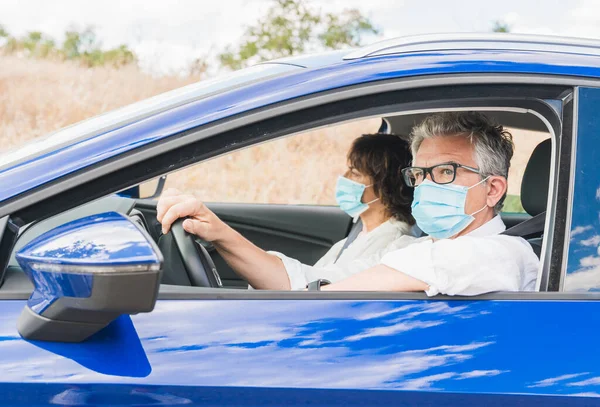 Yeni normal. Tıbbi maskeli bir sürücü bir yolcuyla araba kullanıyor. Sağlık koruması. Arabadaki aile maske güvenliği ve salgın hastalık konseptiyle korunuyor. Coronavirus cihazları. Sosyal uzaklık.