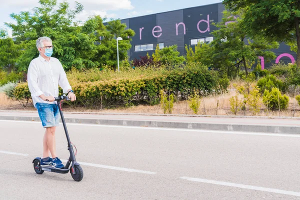 Yeni normal. Elektrikli scooter kullanan maskeli bir adam. Elektirik ve ekolojik taşıma, güvenlik ve salgın konsepti kullanan bir adam. Coronavirus cihazları. Sosyal mesafe. Coronavirüs.