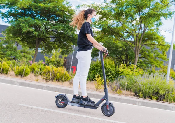Yeni normal. Elektrikli scooter kullanan maskeli genç bir kız. Kadın elektrik ve ekolojik taşımacılık güvenliği ve salgın konseptini kullanıyor. Coronavirus cihazları. Sosyal mesafe. Coronavirüs