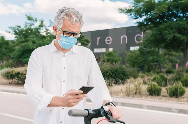 Yeni normal. Cep telefonu uygulamasını kullanarak elektrikli scooter 'ı çalıştıran maskeli bir çocuk. Elektrikli scooter kullanan maskeli bir adam. Elektrik ve ekolojik taşıma kullanan bir adam.