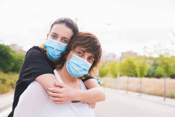 Yeni normal. Aile üyeleri sarılıyor. Koronavirüse karşı korunan anne-kız kucaklaşması. Güvenlik ve salgın konsepti. Coronavirus. Sosyal mesafe. Maskelerle korunan aile.