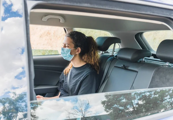Yeni normal. Maskeli bir arabanın arkasında oturan bir ergen. Taksideki genç bir kadın maskeyle korunuyor. Güvenlik ve salgın konsepti. Coronavirus cihazları. Sosyal mesafe. Akıllı telefon kullanan genç kız.